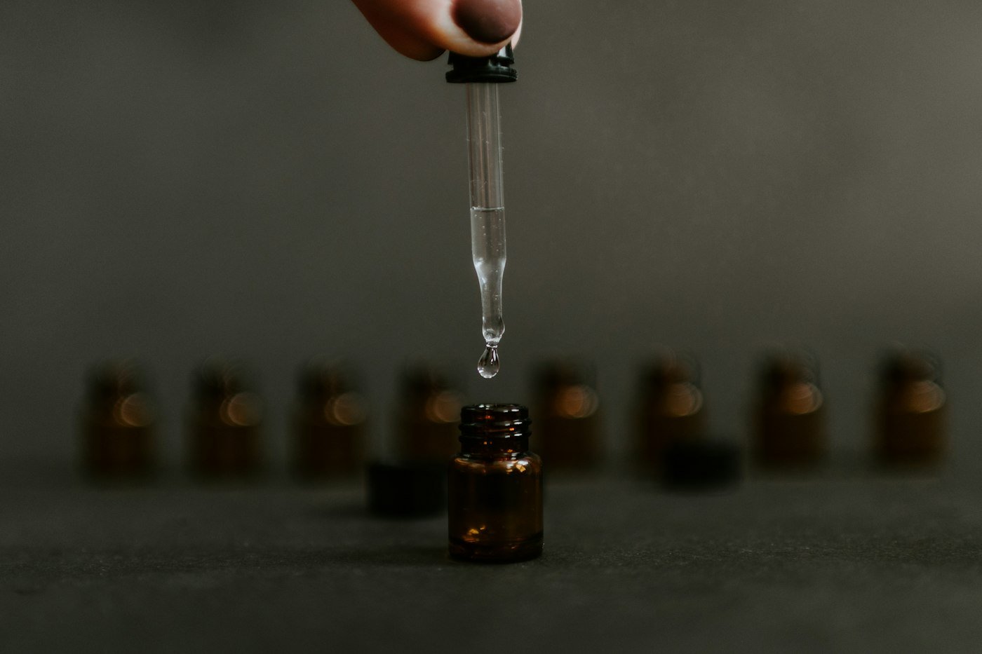 Dropper releasing a drop of oil into an amber glass bottle
