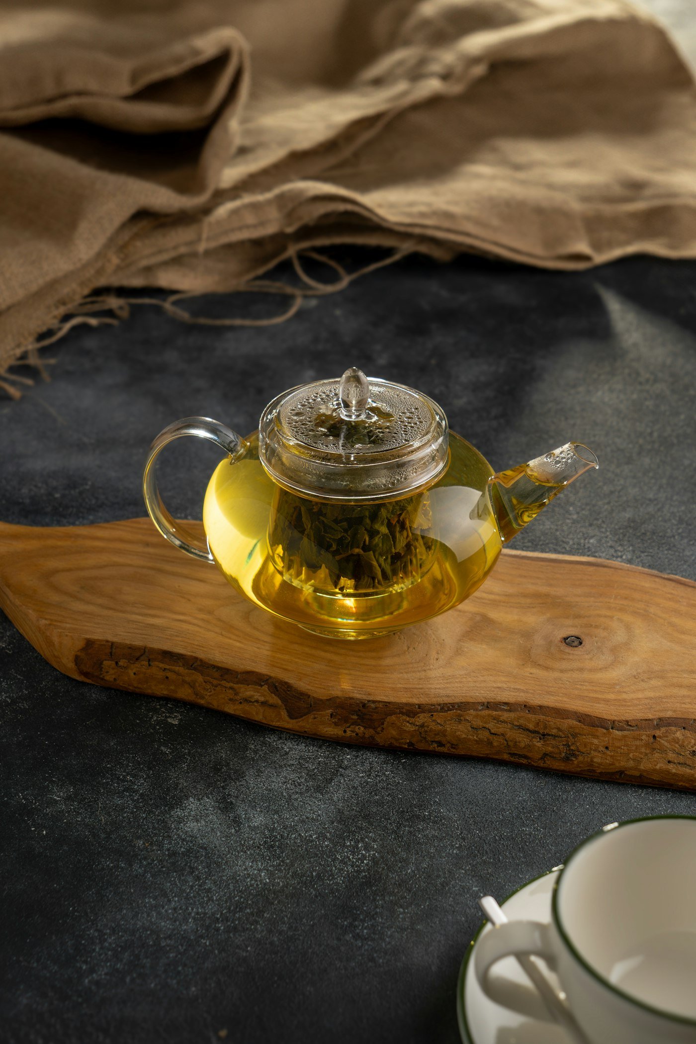 Glass teapot of golden herbal tea on a wooden board